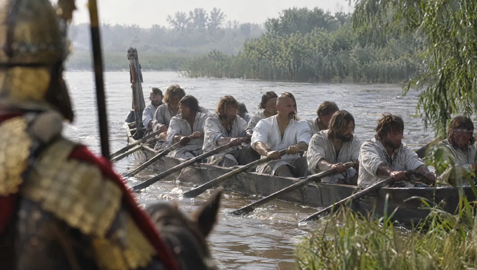 Documentary-style reconstruction of Prince Sviatoslav I rowing with his men in a boat on the Danube in 971, head shaved except for one lock, with a long moustache and a gold earring